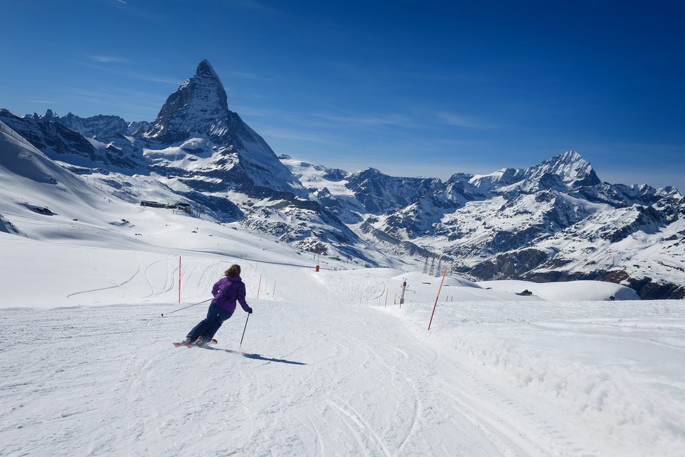 A female skier skiing without a helmet alone on the ski slope towards majestic Matterhorn mountain on a beautiful sunny day with a thick layer of snow in ski resort Zermatt, canton of Valais in Switzerland.