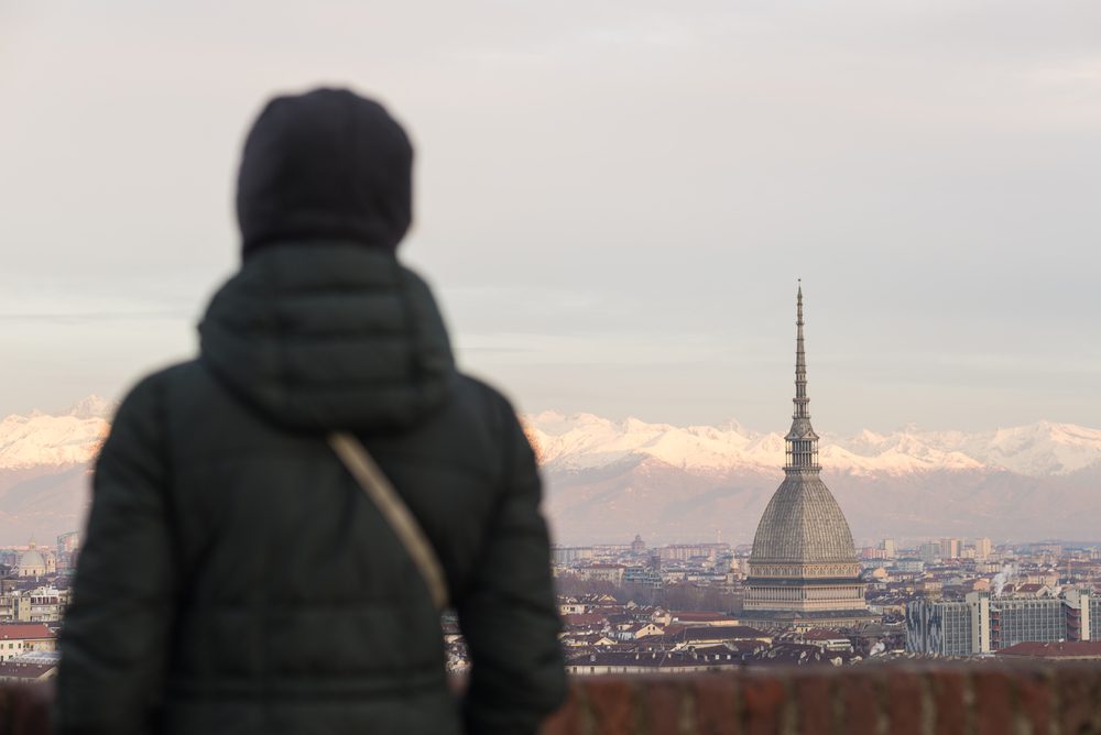 Tourist looking at panoramic view of Torino (Turin, Italy) from balcony above. Winter time, snowcapped Alps in the background. 
