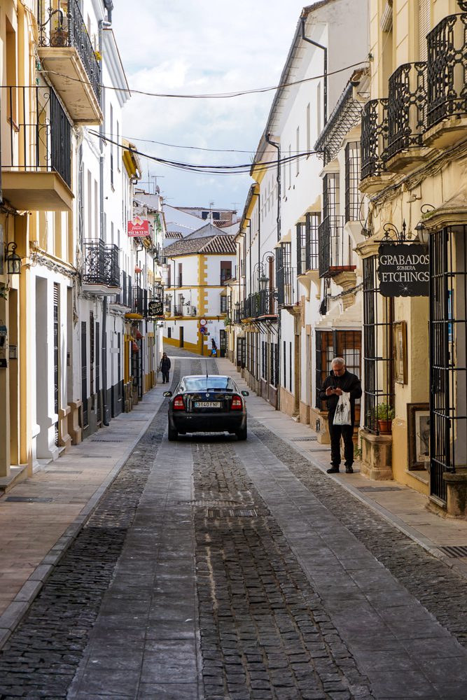 Ronda Spain view of a narrow street with a car, buildings and a man coming out of a shop