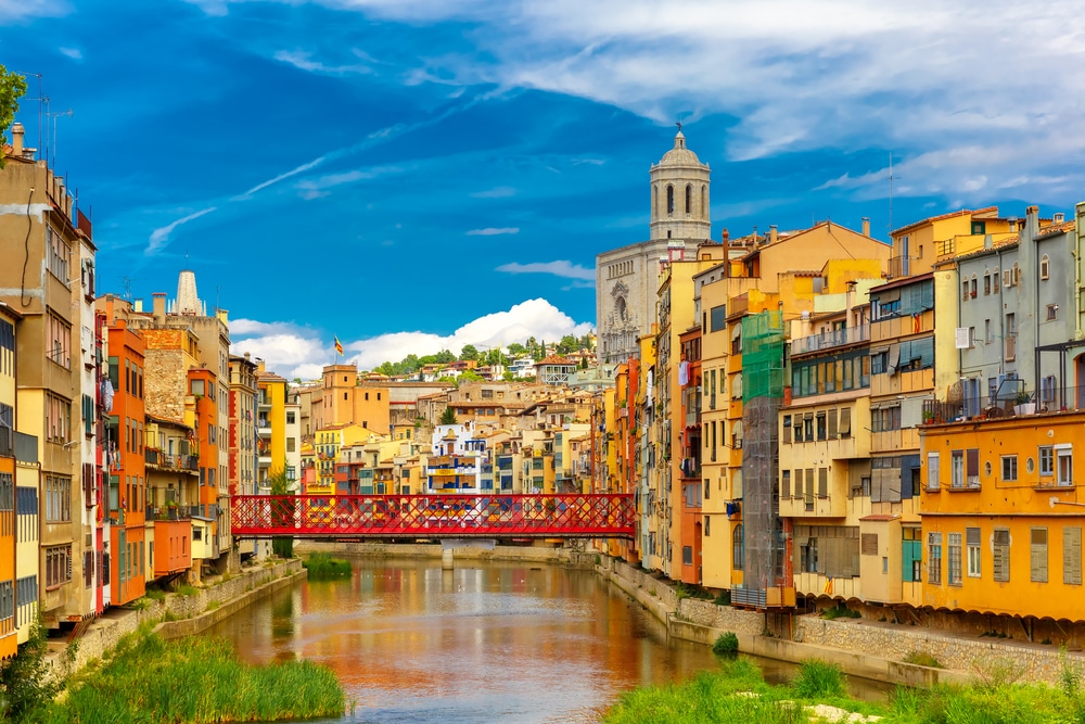 Colorful yellow and orange houses and Eiffel Bridge, Old fish stalls, reflected in water river Onyar, in Girona, Catalonia, Spain. Church of Sant Feliu and Saint Mary Cathedral at background.
