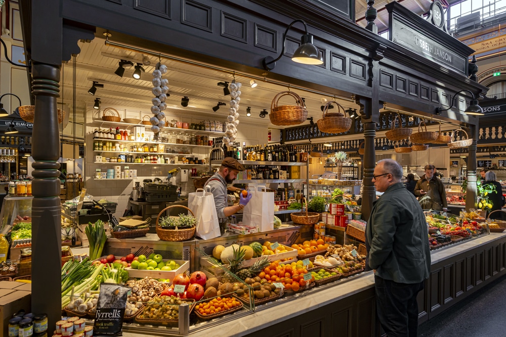 Inside a food market hall in Stockholm. Fruits and vegetables on display with a man shopping