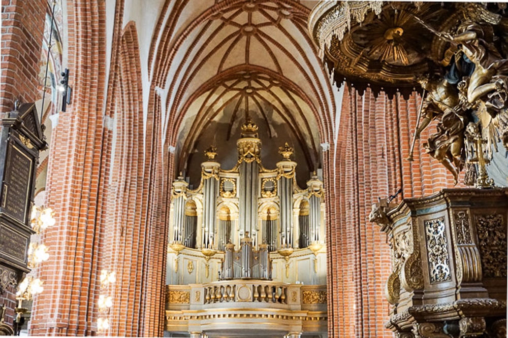 The inside of Stockholm Cathedral. Wooden pulpit in the foreground and pink columns with a curved roof in th background