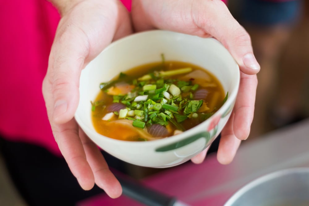 close up of hands holding a bowl of just made Thai soup