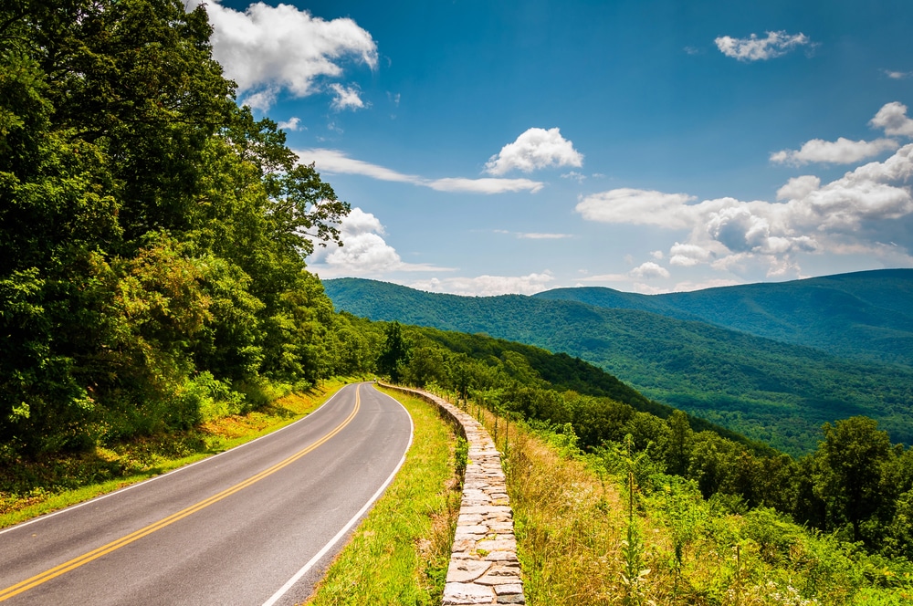 A road with a stone wall on the side and nature and mountains all around