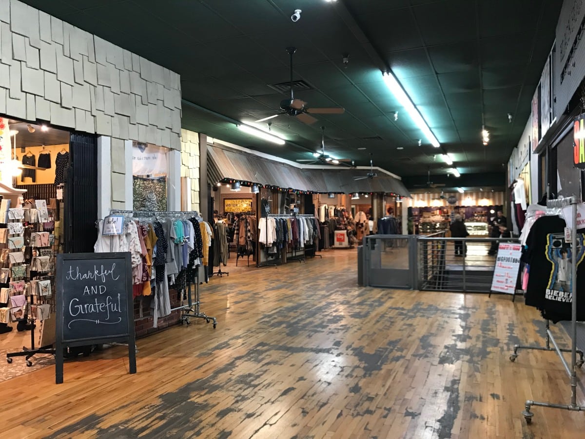 Inside an artisan market in an industrial space. Storefronts visible with signs and clothes hanging in Flagstaff