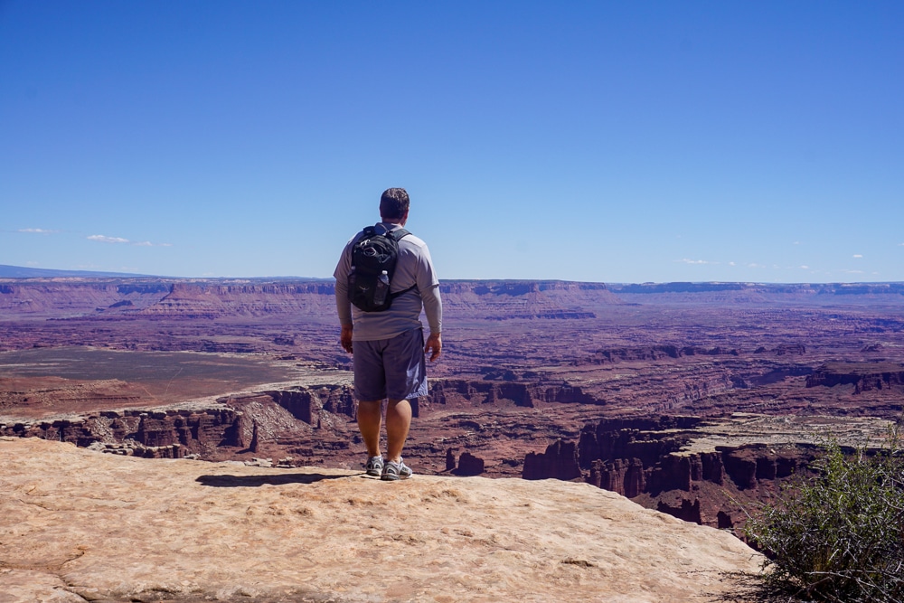 man witha backpack standing on the ledge looking out at Canyonlands National Park in Utah